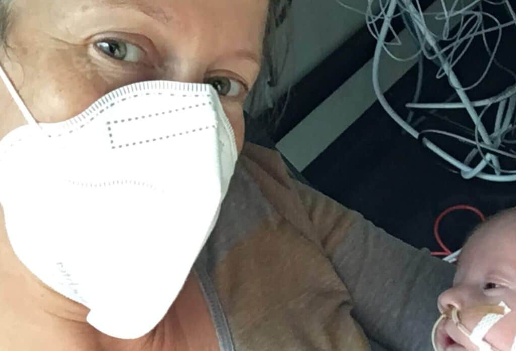 Mutter mit Maske hält Baby mit Beatmung und Nasensonde im Arm