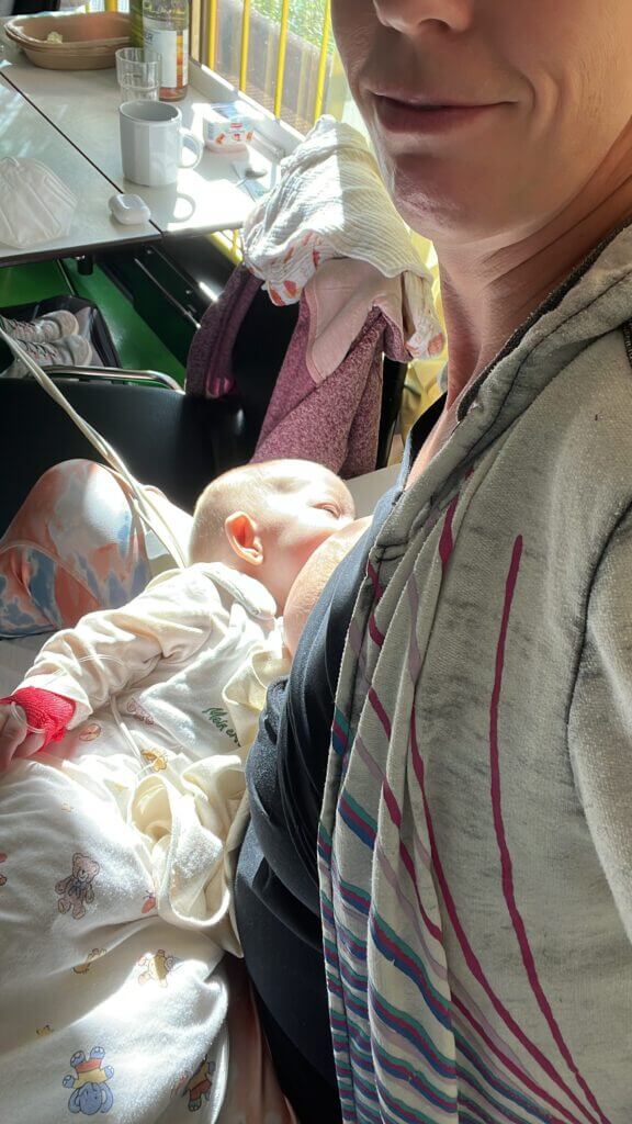 Baby stillt. Monitorkabel sind zu sehen und ein Zugang an der Hand.